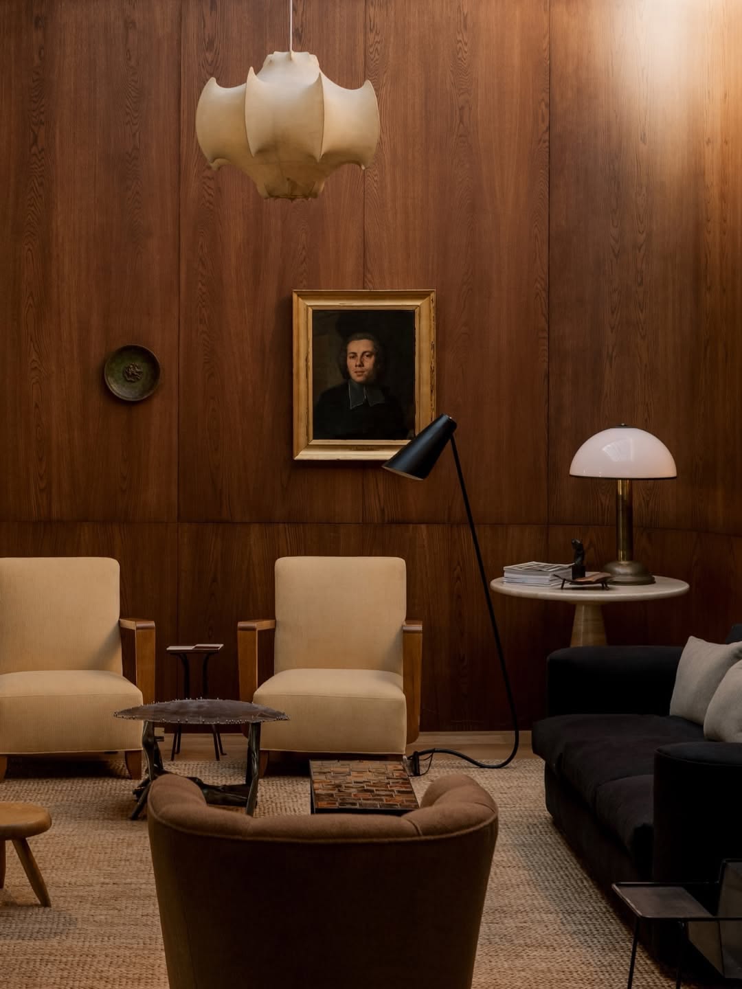 Cocoon pendant lamp above pale armchairs in a wood-panelled room.