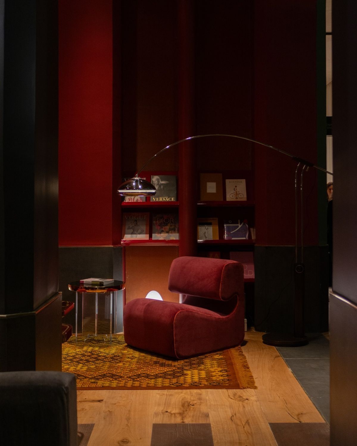 Deep red alcove with a velvet lounge chair, arc floor lamp and a patterned kilim rug.